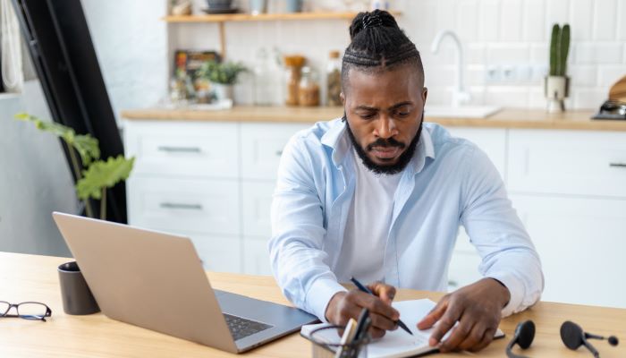 Man writing on notepad while sitting at a laptop